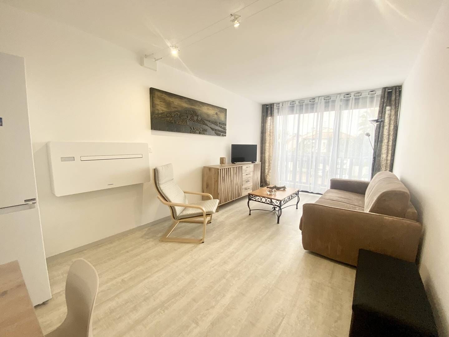 Ein modernes Wohnzimmer mit einer Couch, einem Sessel, einem Couchtisch, einem Fernseher und einem Gemälde an der Wand.