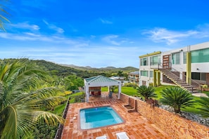 A pool area with a hot tub, a covered seating area, and a view of the surrounding landscape.