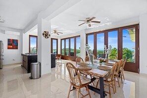 A spacious dining area with a high ceiling, large windows, and a view of the landscape.