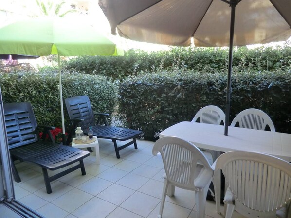 Eine Terrasse im Freien mit Tisch und Stühlen, einem grünen Sonnenschirm und einer Hecke im Hintergrund.