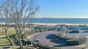 A coastal road with a parking area, a beach, and a lighthouse in the distance.
