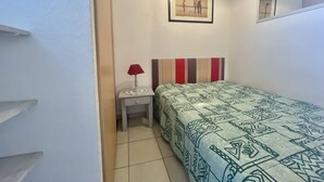 A small, compact bedroom with a bed, a nightstand, a lamp, and a framed picture on the wall.