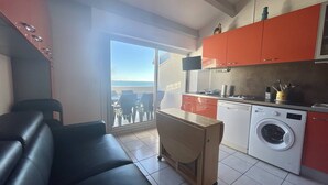 A compact kitchen with a washing machine, a dining area with a table and chairs, and a balcony with a view.