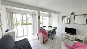 A modern living room with a sofa, a dining table with chairs, a TV, and a balcony with curtains. - CAP D'AGDE / Le Môle : Réf 0073 (CAP D'AGDE)