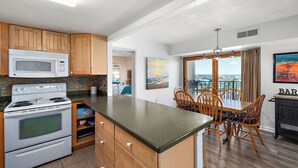 A kitchen with wooden cabinets, a microwave, and a stove. There is a dining area with a table and chairs. - 2 Bedroom Ocean View Condo with Outdoor Pool! (Ocean City)