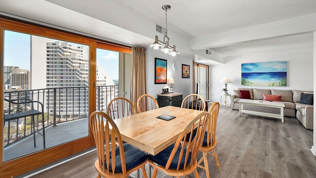 A spacious living area with a wooden dining table, comfortable seating, a sofa, and a balcony with a city view. - 2 Bedroom Ocean View Condo with Outdoor Pool! (Ocean City)