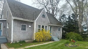 A two-story house with a grey exterior, a front porch, and a small garden with yellow flowers.