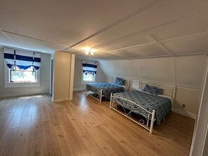 A bedroom with two beds, wooden flooring, and a sloped ceiling. - Sawyer Cove Cottage (Jonesport)