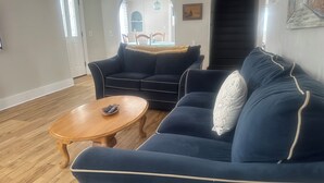 A living room with a dark blue sofa, a wooden coffee table, and a dining area in the background.
