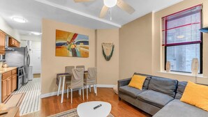 A modern living room with a grey sofa, a small white table, and a dining area with chairs. - Amazing Columbus Circle & Central Park 3-Bedroom by ~ Queen Beds ~By Metro ~ W/D (New York)