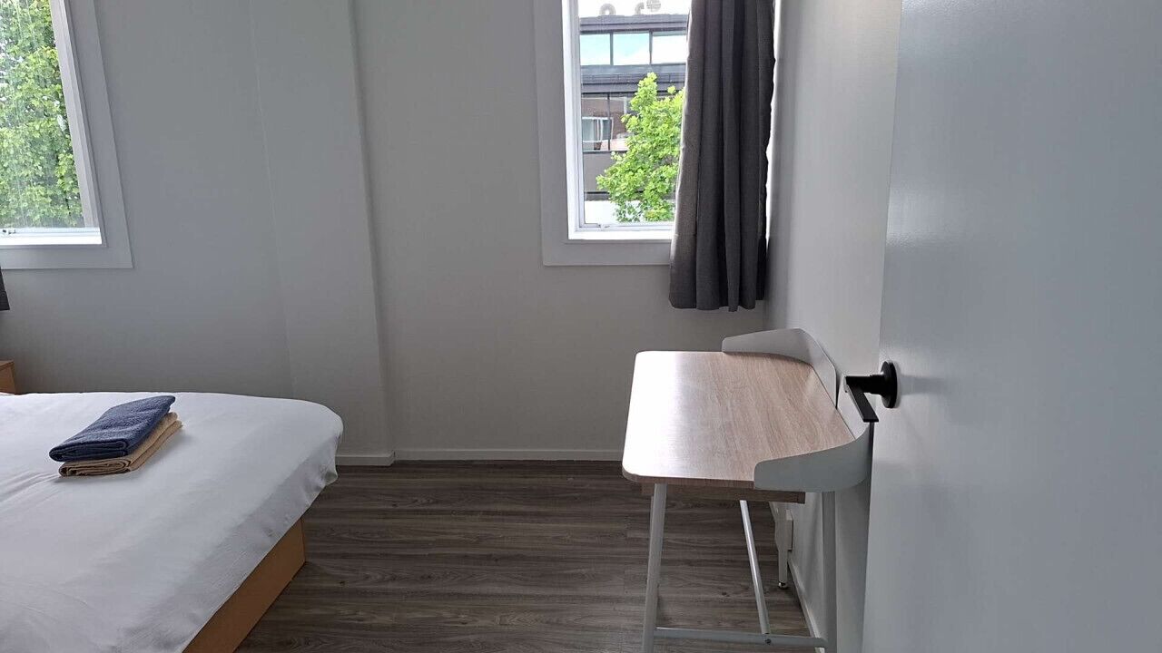 A bedroom with a bed, a chair, and a window with curtains.