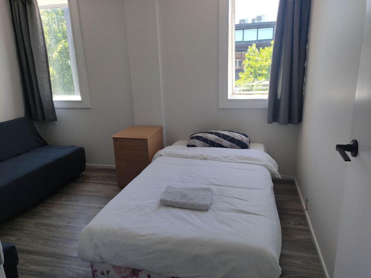 Une pièce comprenant un lit, un canapé, une petite commode en bois et une fenêtre avec des rideaux.