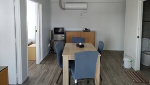 Une pièce de taille modeste comprenant une table à manger en bois, des chaises bleues, un four à micro-ondes, un petit coin cuisine et un ventilateur de plafond.