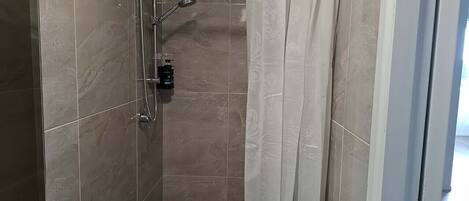 A shower with a handheld showerhead and a wall-mounted faucet, tiled walls, and a curtain.
