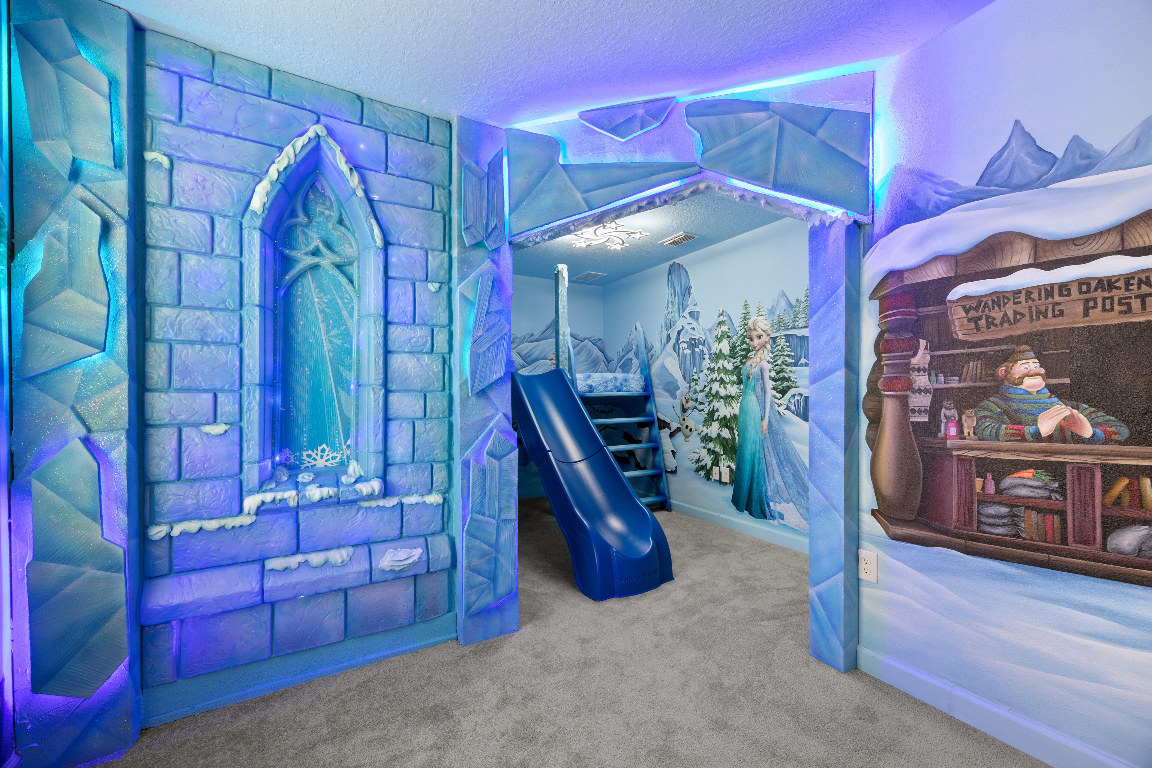 Una habitación con pared decorada en tonos azules con motivos de hielo, un tobogán pequeño de color azul y un mural de una estación de trueque.