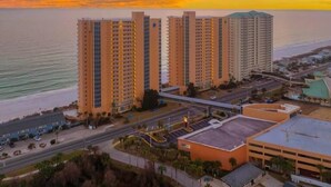 Un grand hôtel à plusieurs étages, doté d’un parking et offrant une vue sur l’océan au coucher du soleil.
