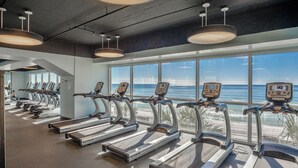 Un gimnasio con cintas de correr frente a un ventanal con vistas a la playa.