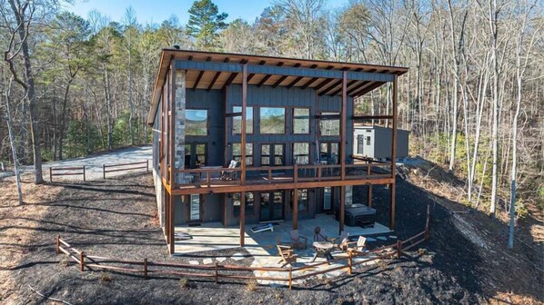 A two-story cabin with a balcony, surrounded by a wooden fence and a forested area.