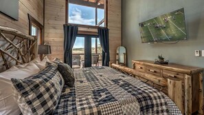 A cozy bedroom with a large bed, wooden dresser, and a TV mounted on the wall.