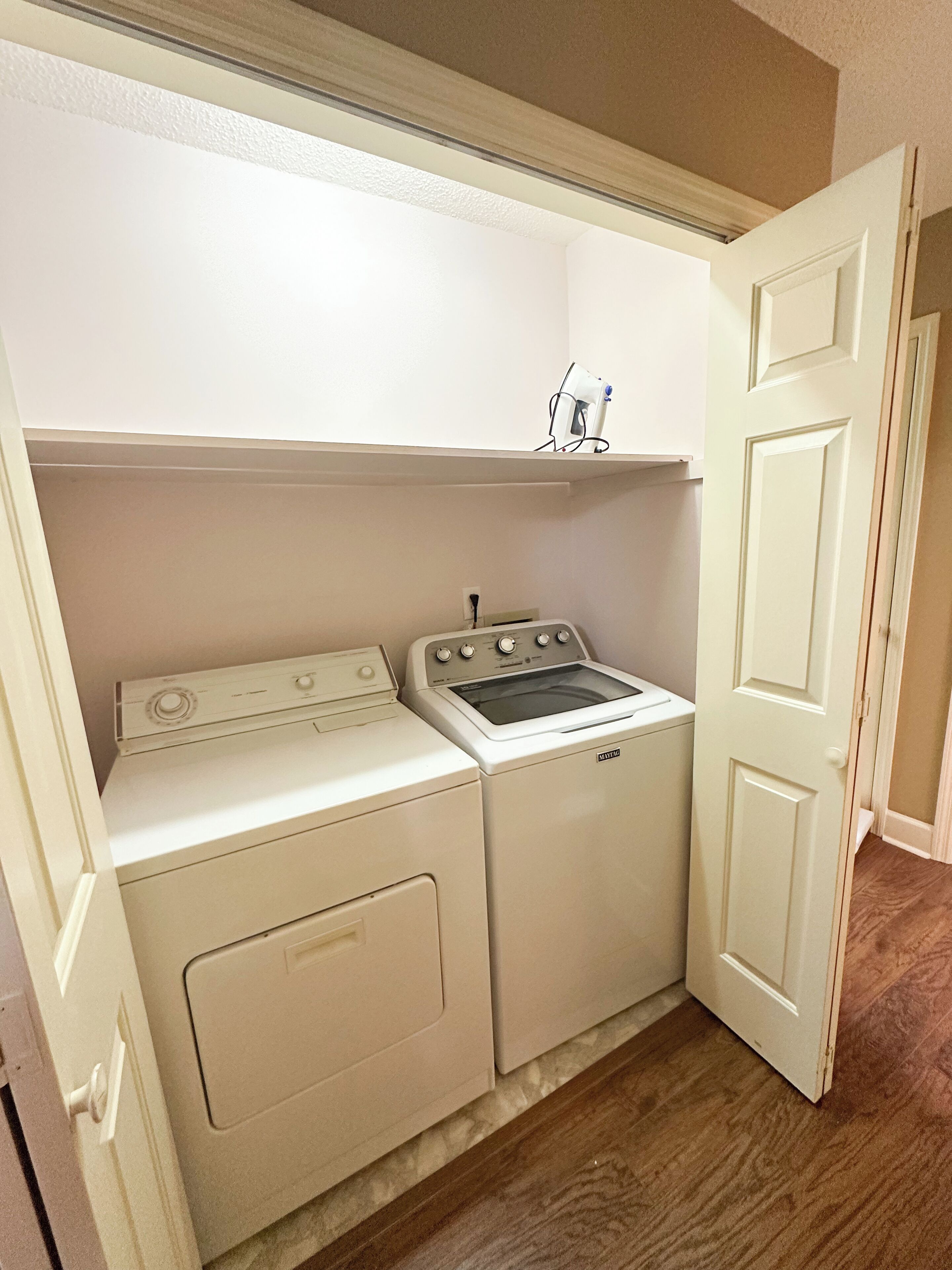 A laundry room with a washer and dryer, a small shelf above the dryer, and a door leading to another room.