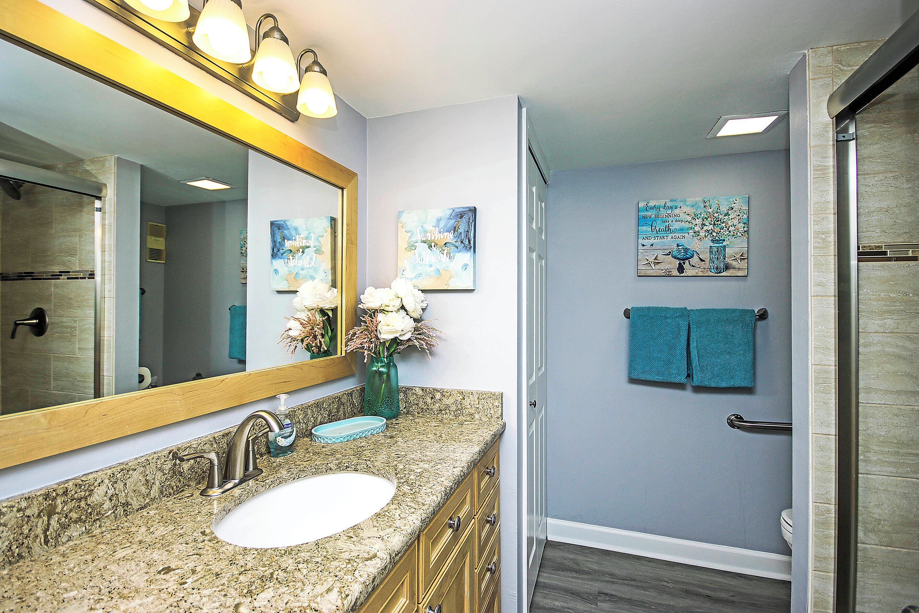 A bathroom with a granite countertop sink, a large mirror, and a shower area.