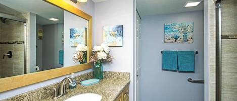 A bathroom with a granite countertop sink, a large mirror, and a shower area.