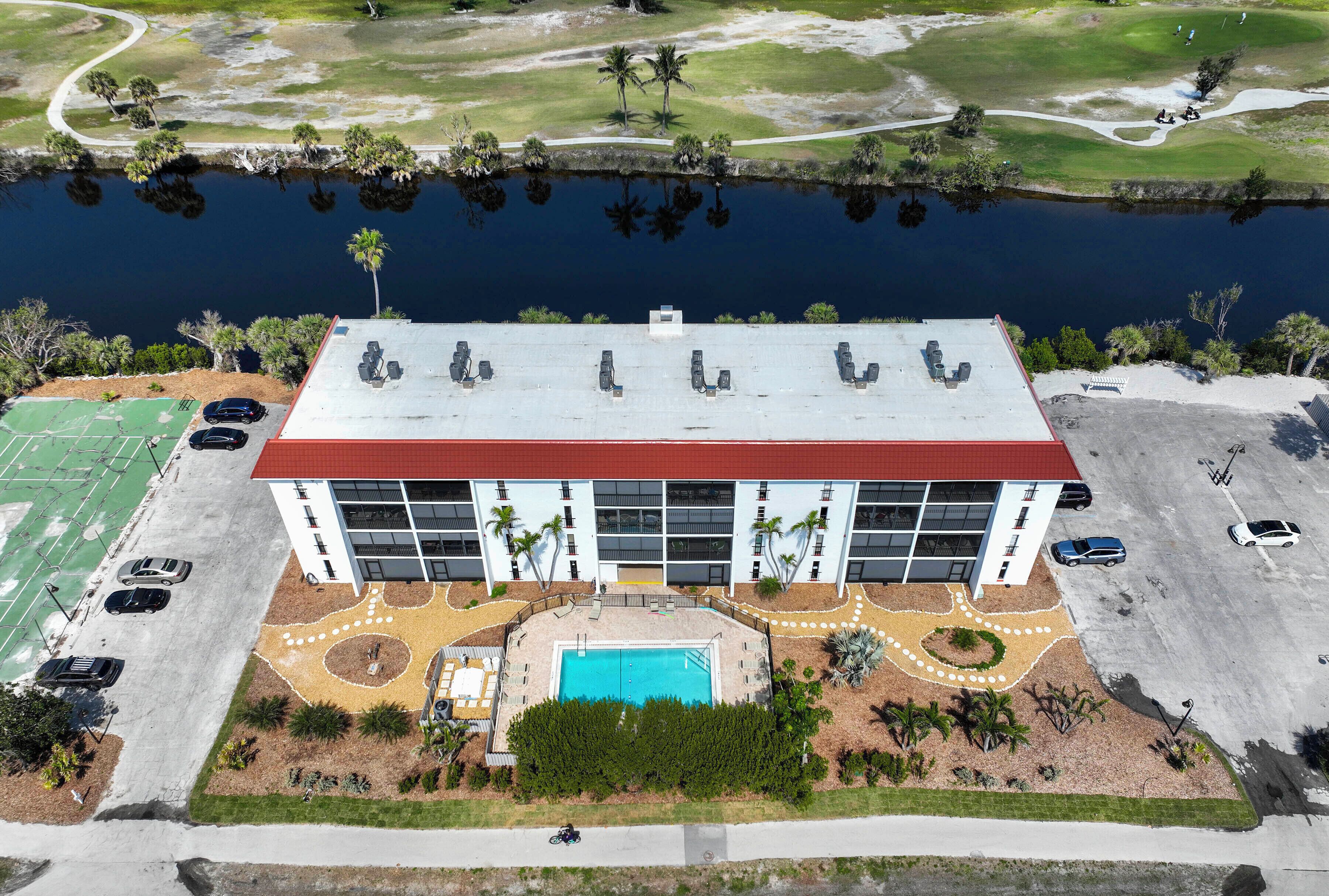 An aerial view of a building with a swimming pool, surrounded by palm trees and a golf course.