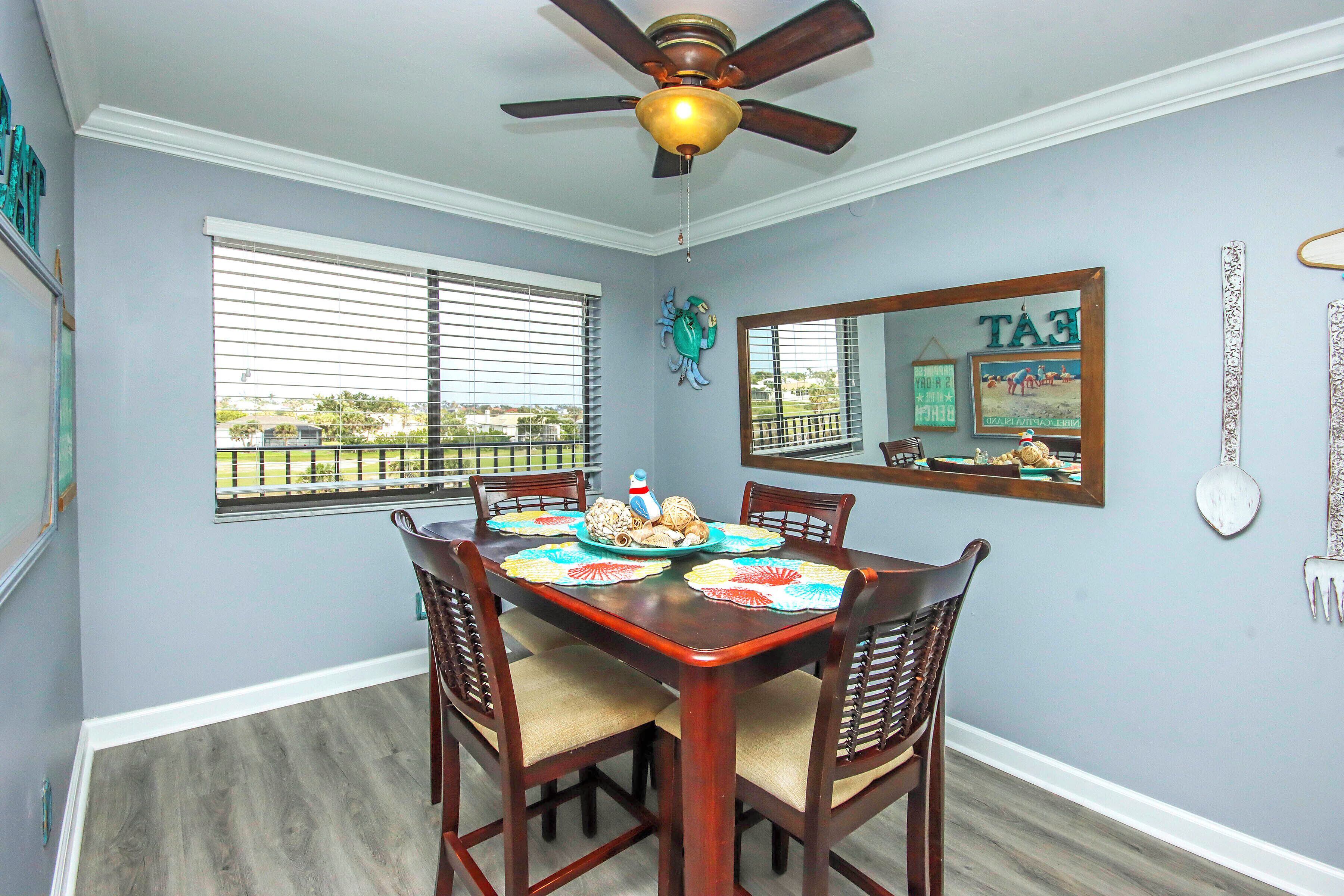 A dining room with a wooden table, four chairs, a ceiling fan, and a window with blinds.
