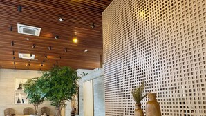 Un interno moderno con soffitto in legno, una pianta grande e un'area salotto con divani e poltrone.