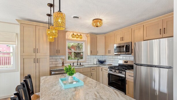 A modern kitchen with light wood cabinets, stainless steel appliances, a marble island, and pendant lighting. - 5206 Hogg Heaven * 3 Min Walk to Beach (Kill Devil Hills)