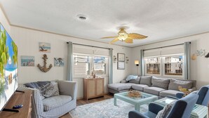 A living room with a striped sofa, a grey sectional, a glass coffee table, and a ceiling fan. - 5206 Hogg Heaven * 3 Min Walk to Beach (Kill Devil Hills)