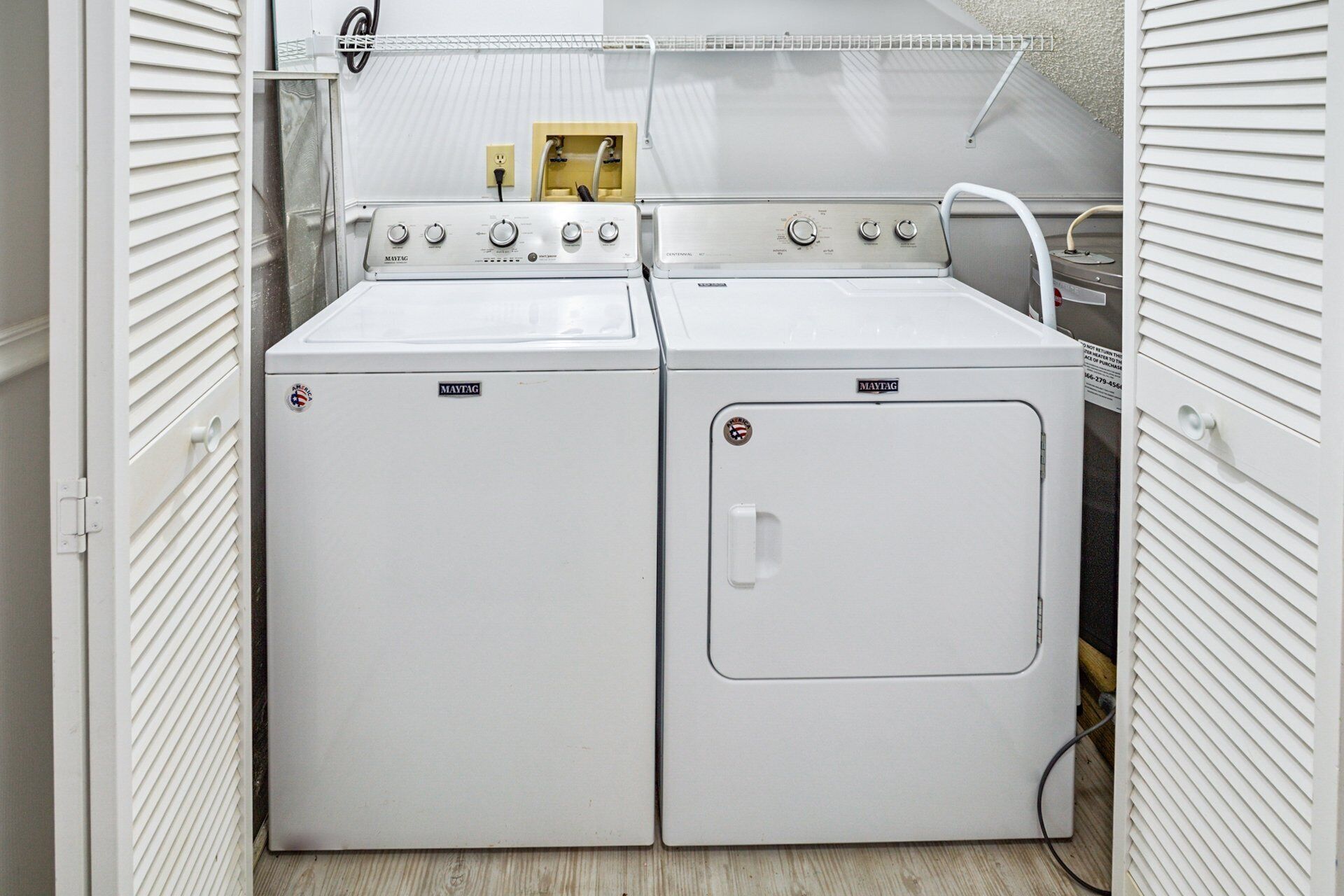 Een wasserette met twee Maytag wasmachines en drogers, een metalen plank erboven en een stopcontact.