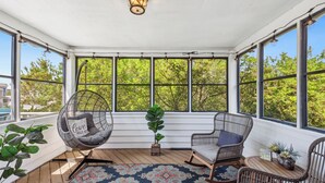 Une véranda abritée avec un fauteuil suspendu, deux fauteuils à bascule, un tapis à motifs et une plante en pot.
