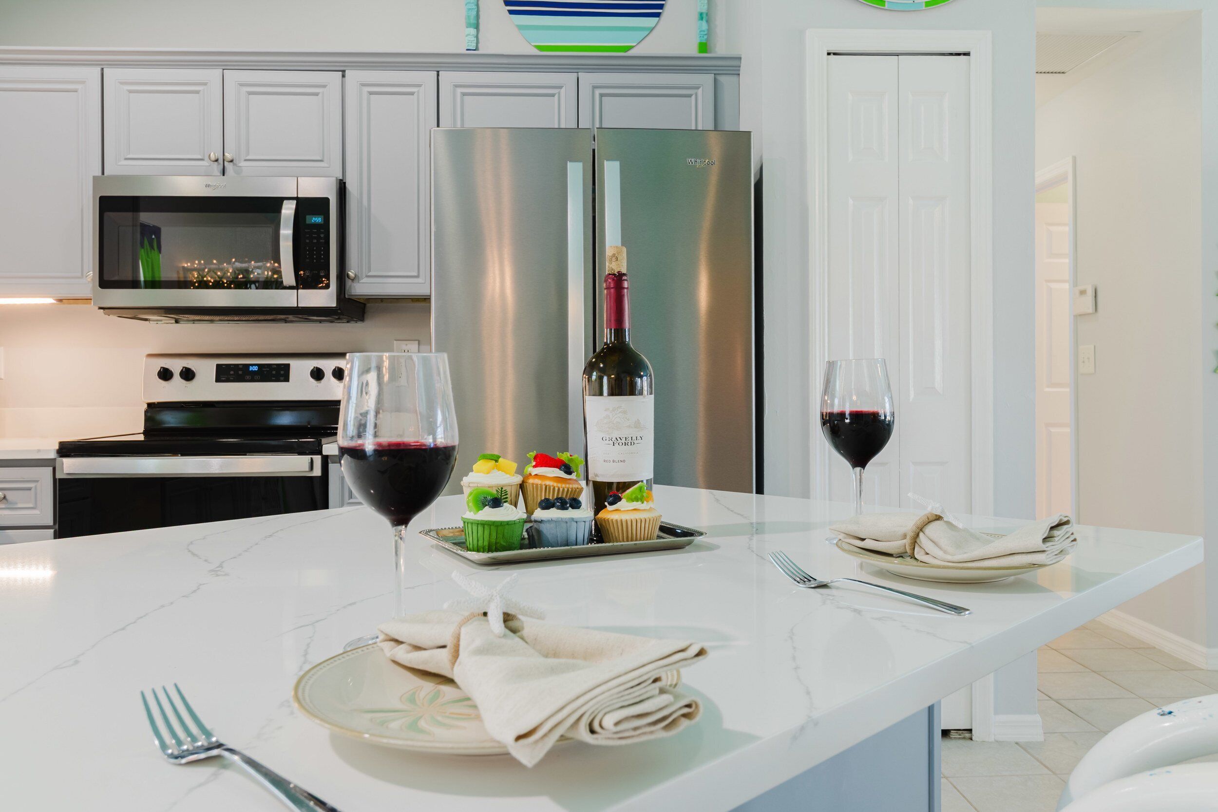 A kitchen with white cabinets, a stainless steel refrigerator, a microwave, and a wine bottle on the counter.