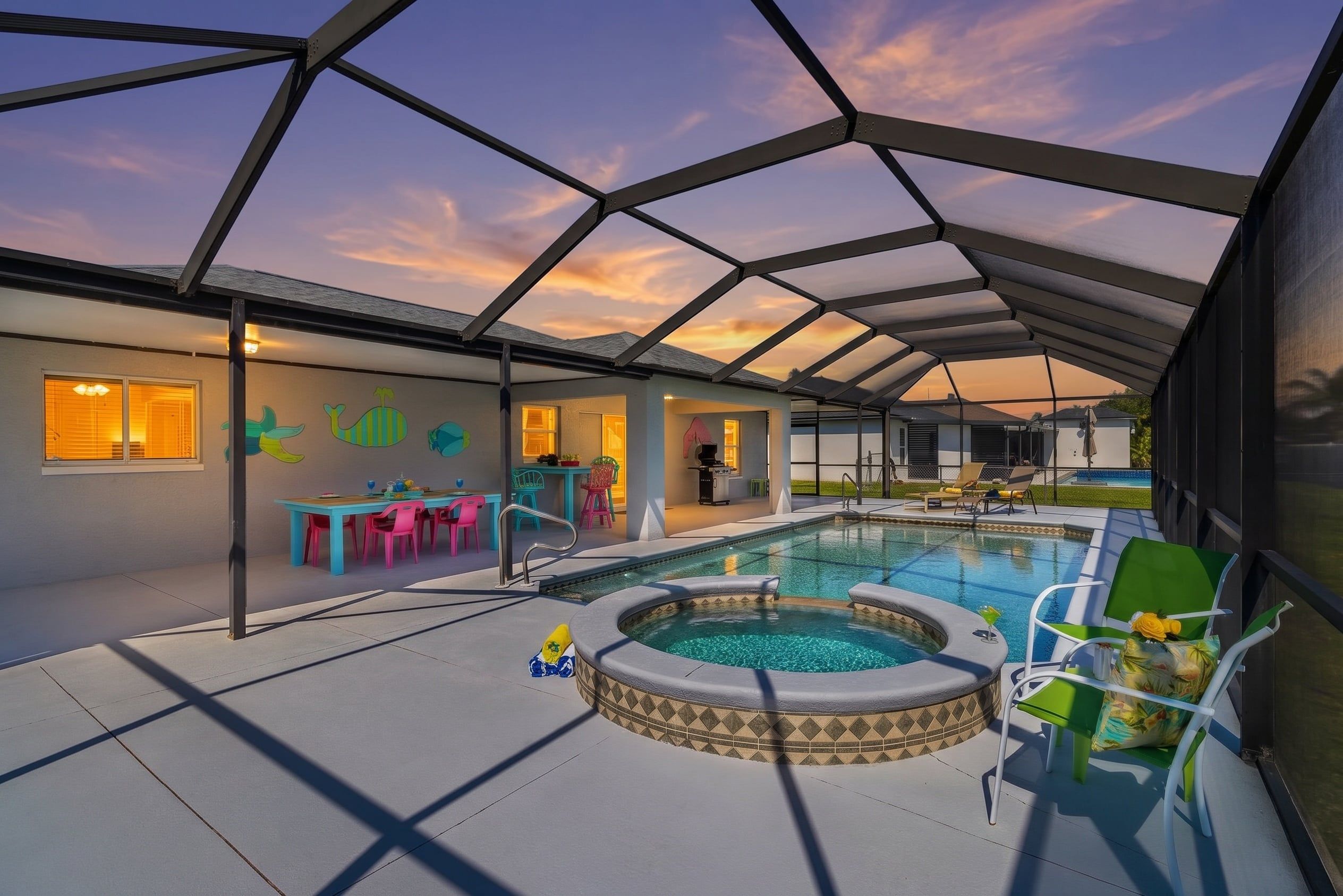 A covered outdoor swimming pool area with a hot tub, seating, and a dining area with colorful chairs.
