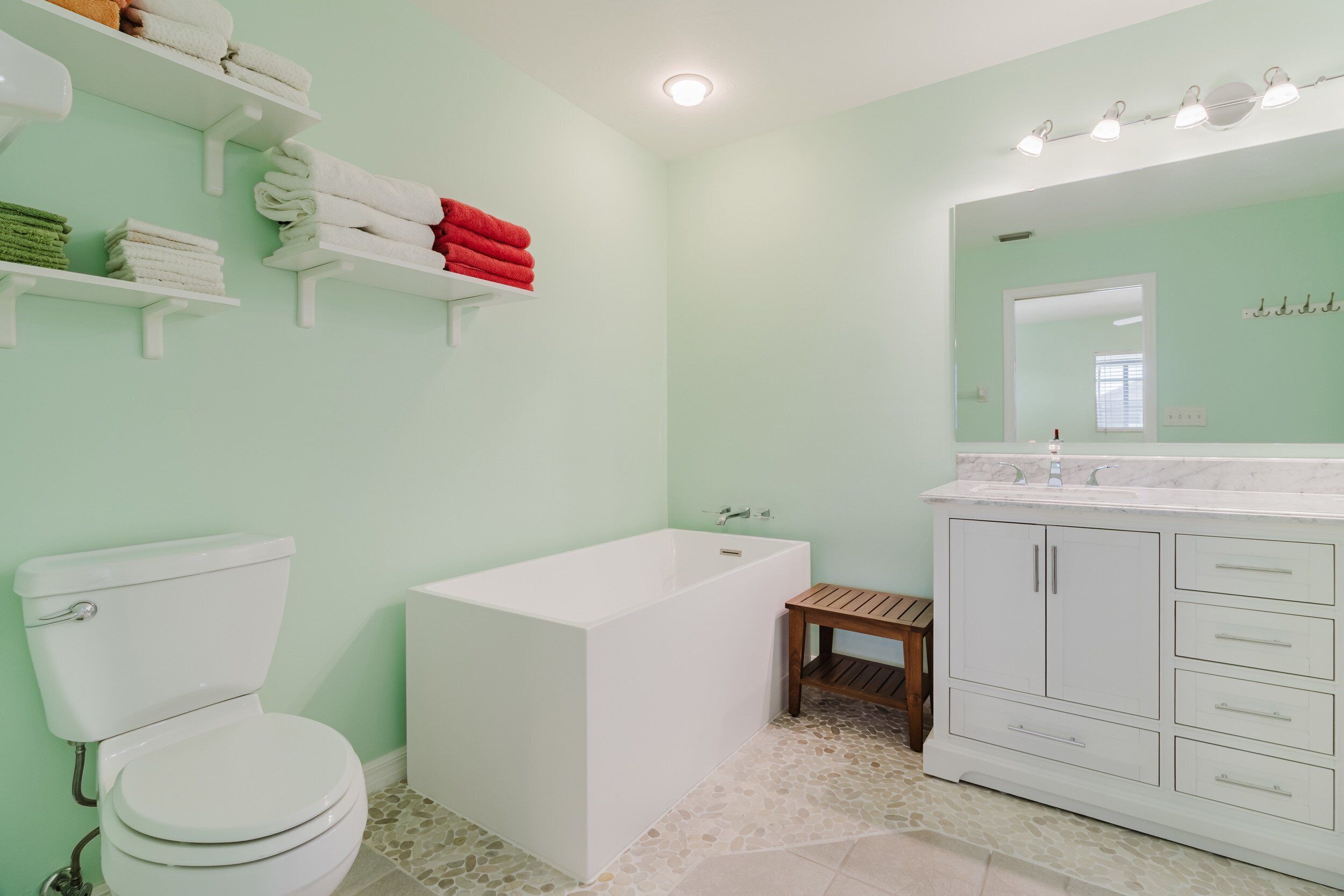 Ein Badezimmer mit Toilette, Badewanne, einem hölzernen Hocker und einem Waschtisch mit Schubladen und Spiegel.