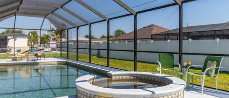 A covered outdoor swimming pool with a hot tub, surrounded by chairs and a fence.
