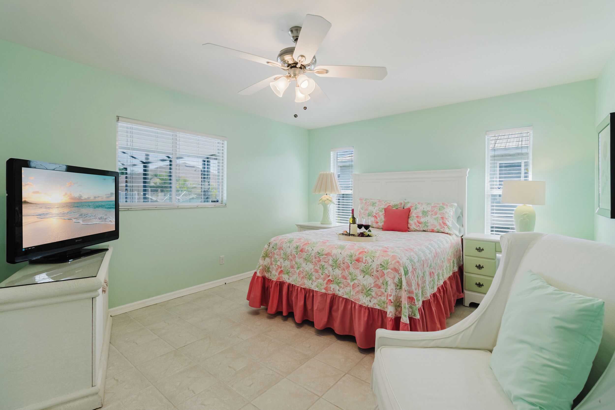 A bedroom with a bed, a television, a ceiling fan, and a window with blinds.