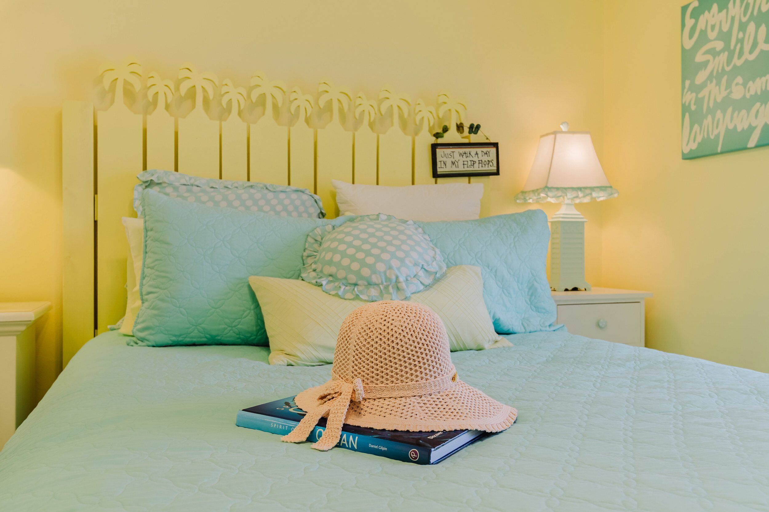 A neatly made bed with a blue quilt, a crocheted hat, and a book.