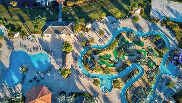 Vista aérea de un resort con una piscina grande, un tobogán de agua y un campo de golf.