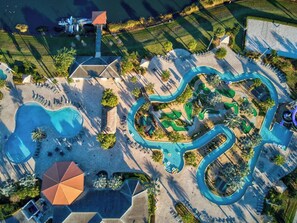 An aerial view of a resort with a large swimming pool, a water slide, and a golf course.