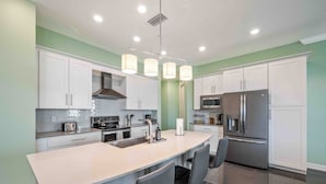 Una cocina moderna con armarios blancos, una isla grande con taburetes de bar, electrodomésticos de acero inoxidable e iluminación colgante.