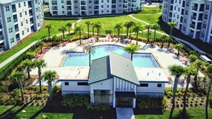 Un moderno complejo hotelero con varias construcciones, un área de piscina central con sillas de descanso y jardines bien cuidados.