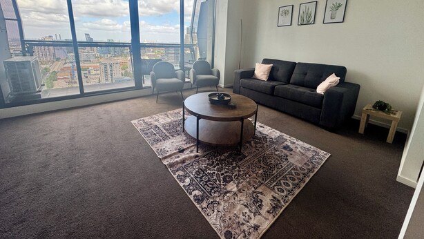 Een moderne woonkamer met een groot raam, een bank, twee fauteuils, een salontafel en een kamerkleed met dessin.