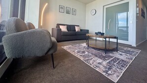 Een moderne woonkamer met een grijze bank, een ronde salontafel en een kamerbreed tapijt met dessin.