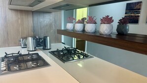 Een keuken met een gasfornuis, een waterkoker en een koffiezetapparaat. Boven het fornuis staan planten in potten.