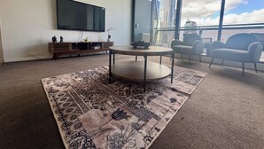 Een moderne woonkamer met een grote televisie, een ronde tafel en een kamerkleed met dessin.