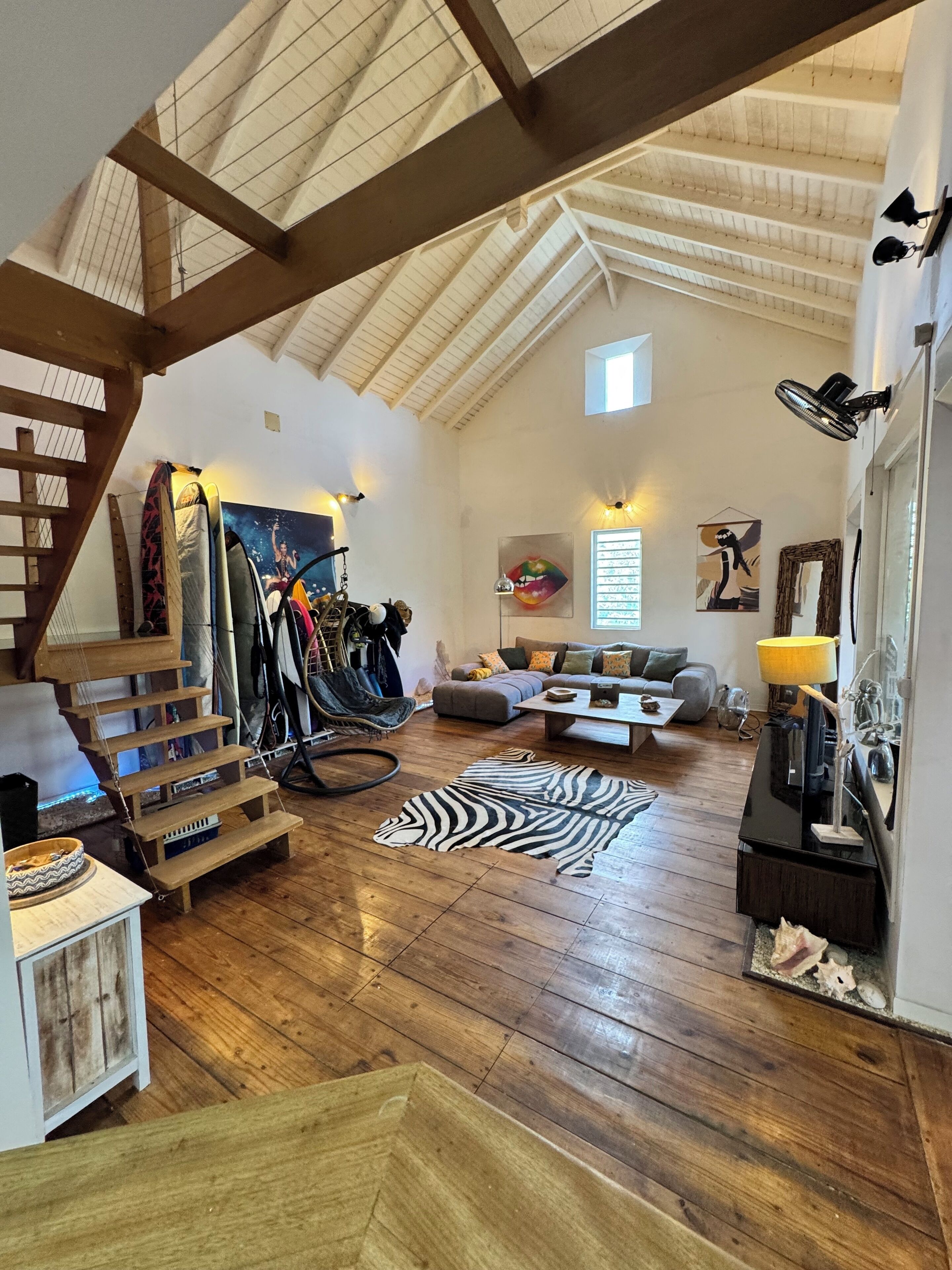 A spacious loft with high ceilings, exposed wooden beams, a staircase, a zebra print rug, a sofa, and a dining area.