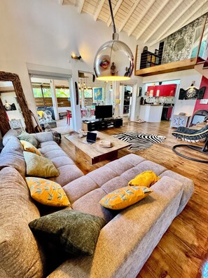 A spacious living area with a large sofa, a coffee table, and a television. There is a kitchen area visible in the background. - El Poyito Kite & Surf Camp | room La Désirade (Sainte-Anne)