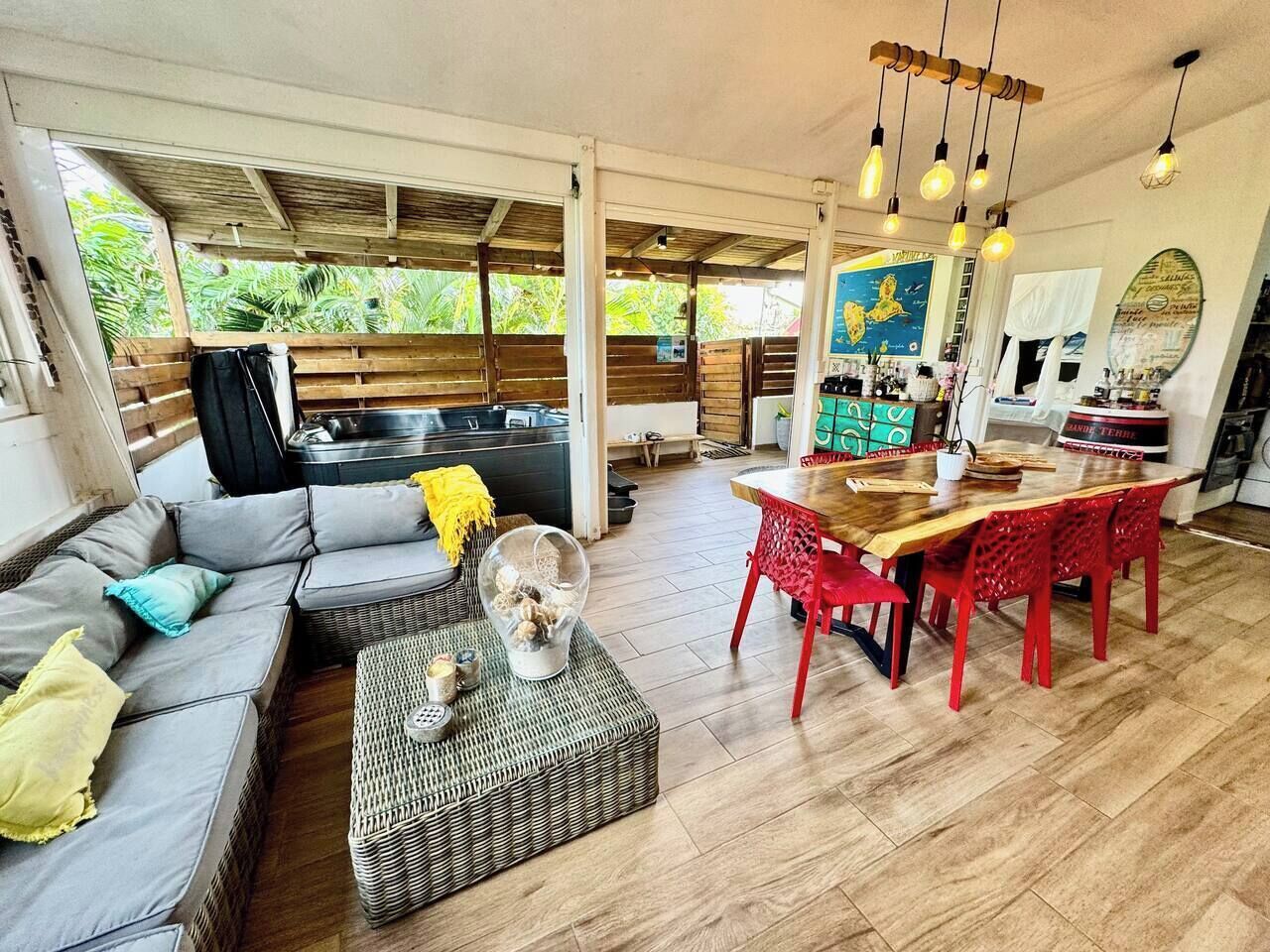 A spacious living area with a sofa, a dining table with red chairs, and a kitchen area with a counter and various items.
